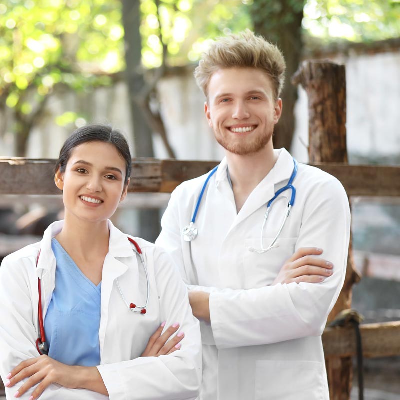 Arzt und Ärztin stehen mit verschränkten Armen lächelnd zur Kamera